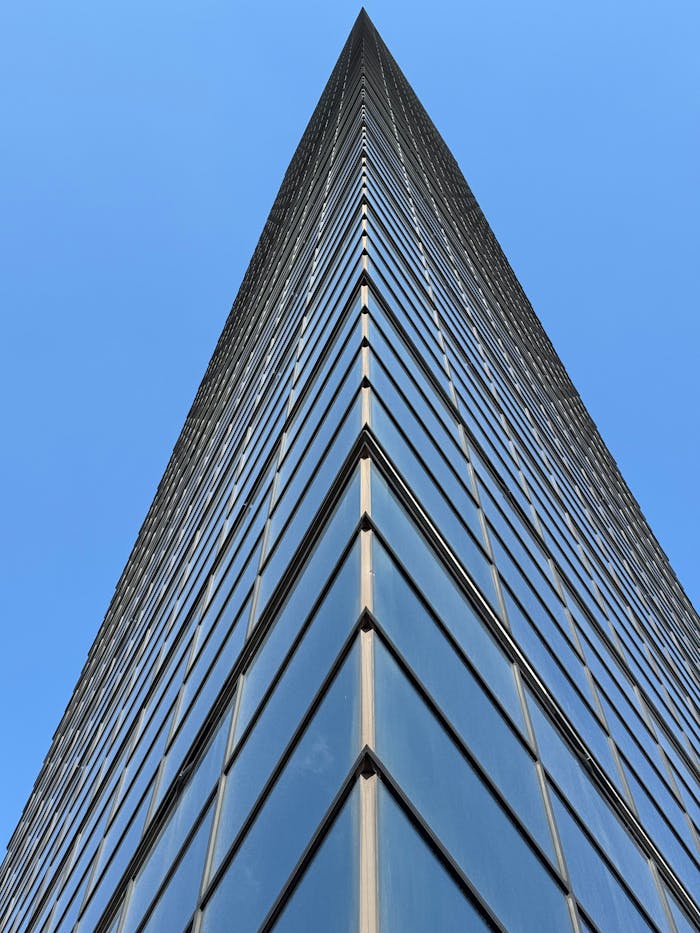 Low angle view of a contemporary glass skyscraper against clear blue sky, showcasing architectural symmetry.
